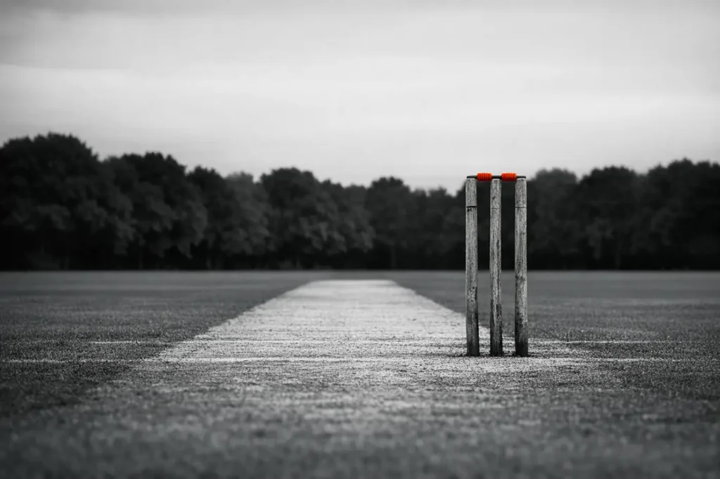 Wooden cricket stumps with red bails on an empty ground, sports spread betting on runs, goals and margins